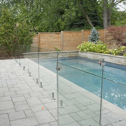 Code-compliant frameless glass pool fencing with stainless steel spigots and glass-to-glass corner clamps around a residential pool