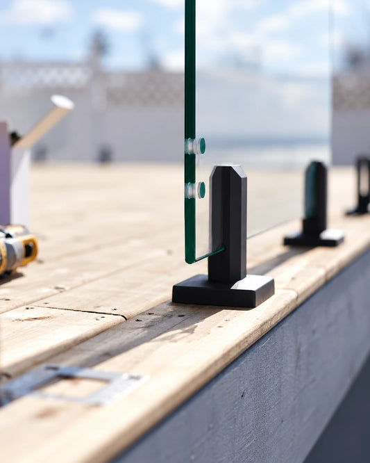 Gate support glass panel with two hinge holes, held by a matte black spigot on a wood deck