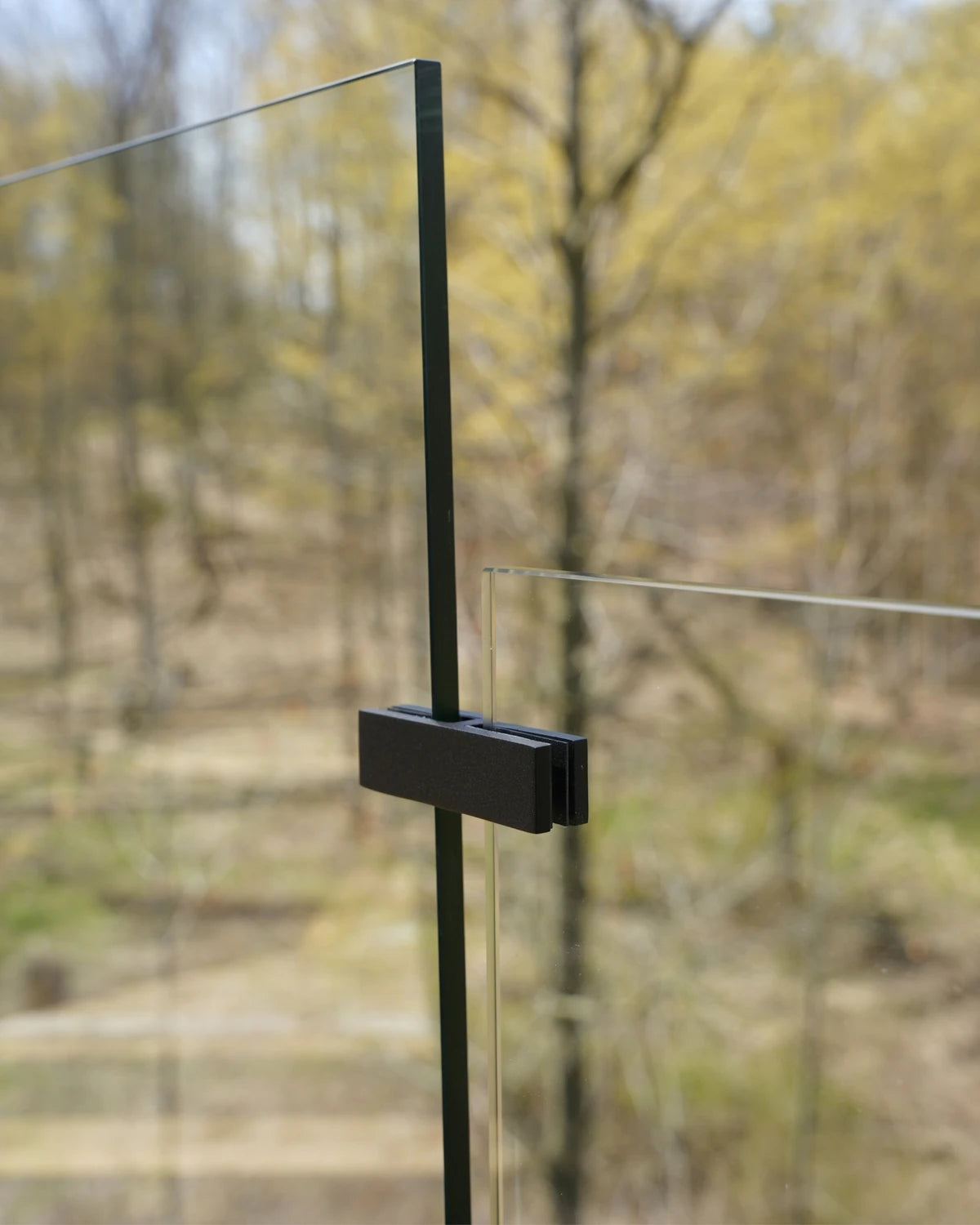 Matte black 180° glass-to-glass connector joining two frameless glass railing panels