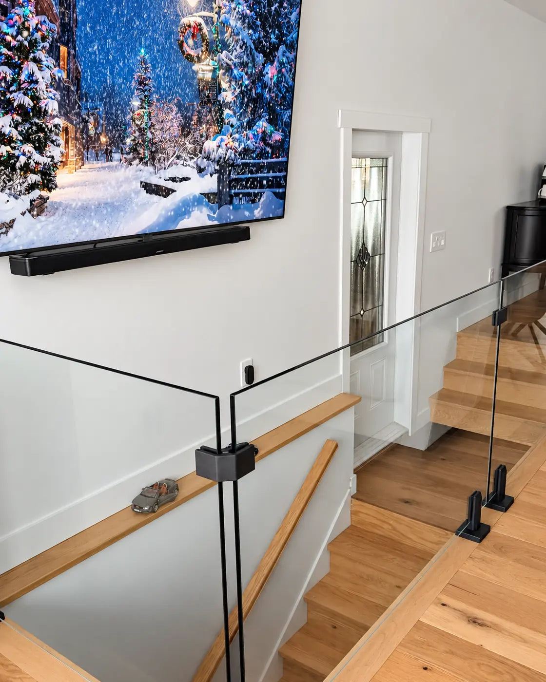 Matte black 90° corner connector joining two 12mm glass railing panels around an indoor stairwell opening