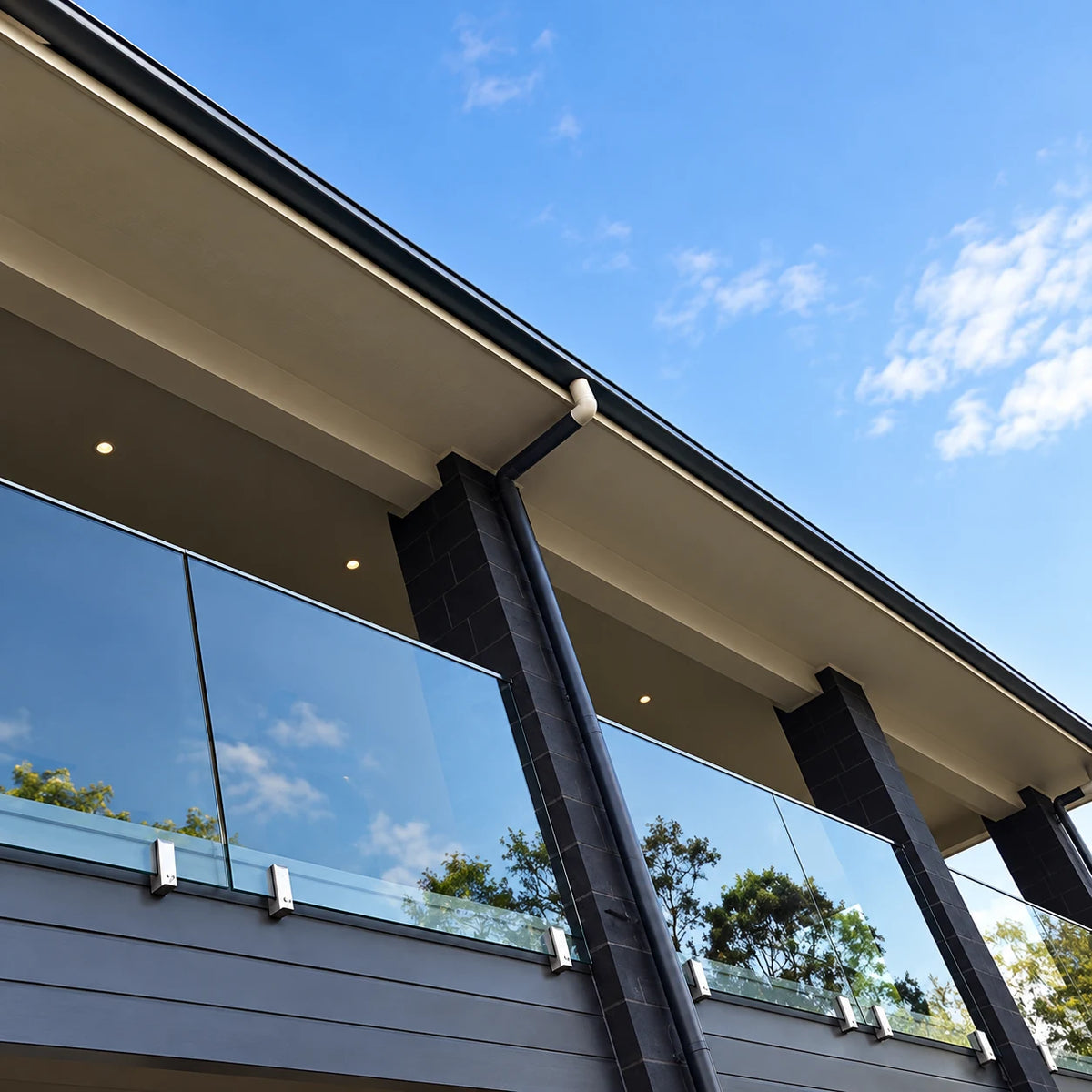 Modern glass balcony railing secured with stainless side-mount fascia spigots on a contemporary home with dark exterior cladding.